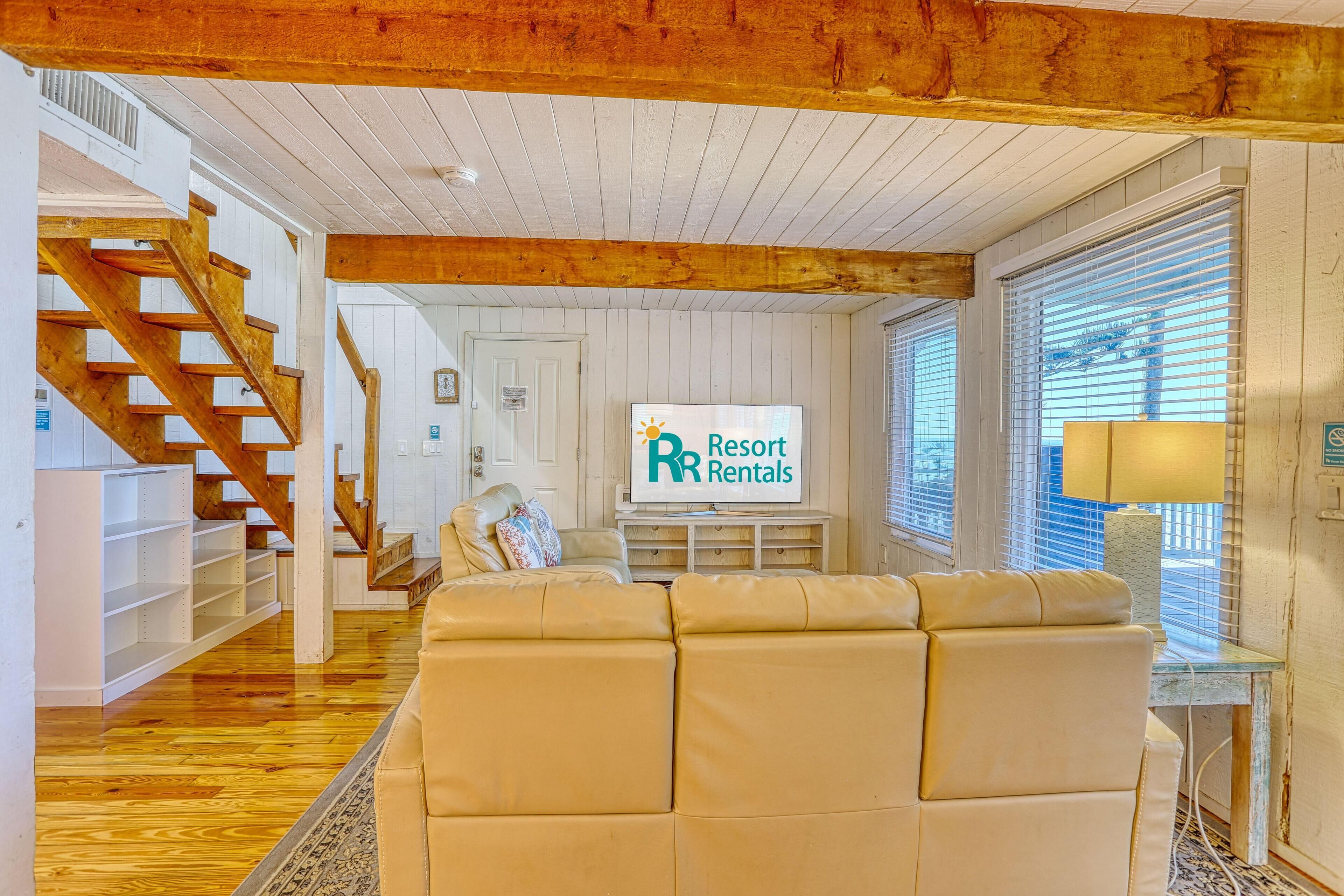 A spacious living room with a large beige sofa, wooden staircase, and a sign for 'Resort Rentals'.