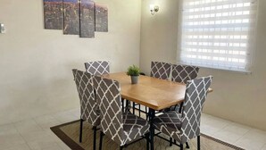 A dining area with a wooden table and patterned chairs, a potted plant, and a cityscape artwork on the wall. - Safe & Spacious 2 BR Apt, Budget Friendly on South
 (Oistins)