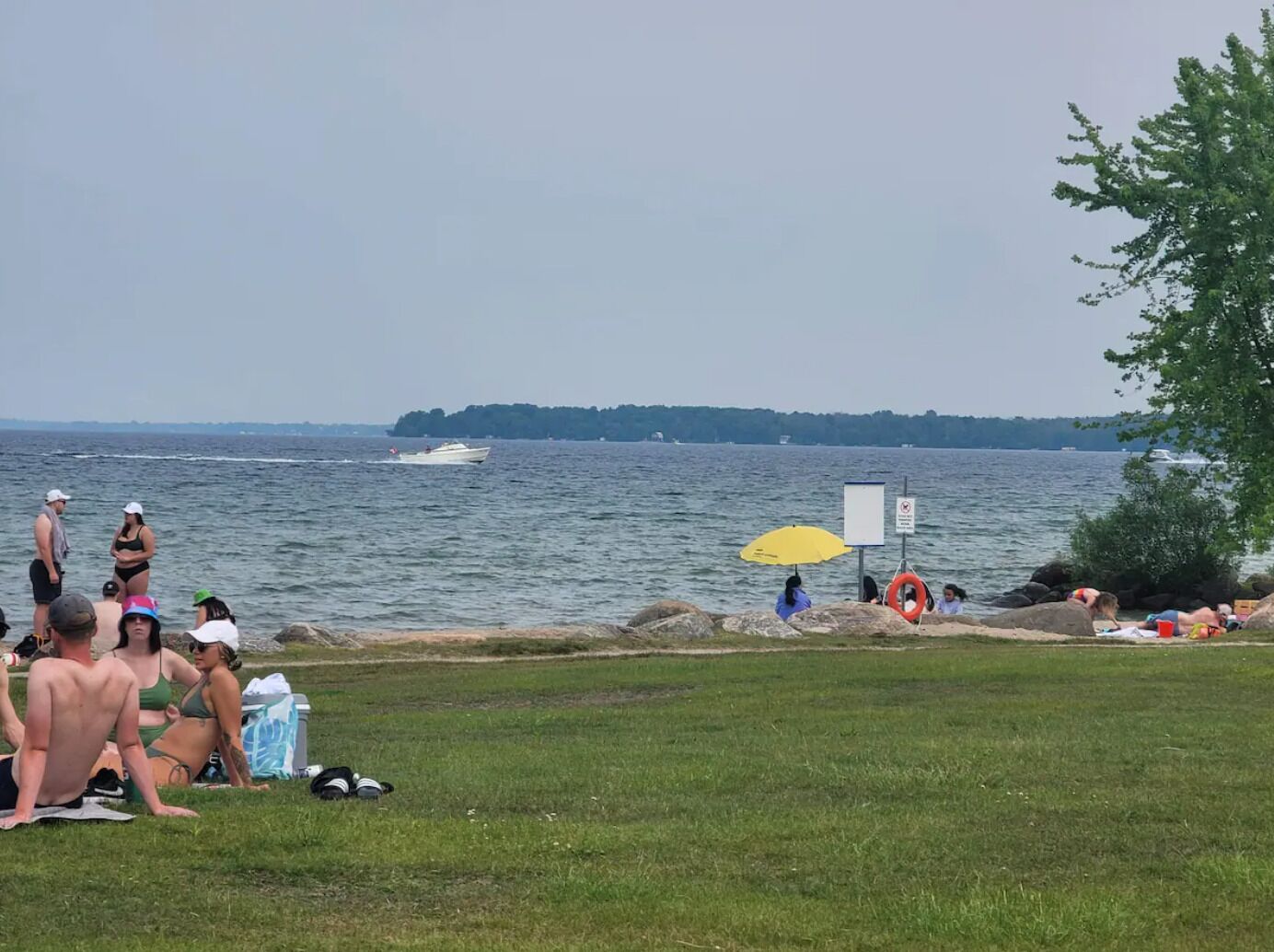 A grassy area with people relaxing near a body of water, a boat, and a lifebuoy.