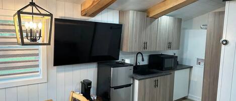 A compact kitchen with a flat-screen TV, a coffee machine, and wooden cabinets.