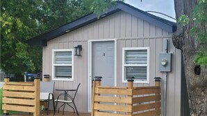 A small, single-story building with a porch, two windows, and a door.