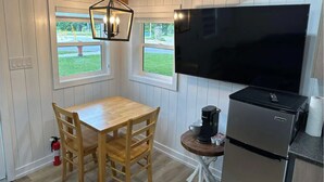 A compact kitchen with a wooden dining table, a coffee maker, a refrigerator, and a large TV.
