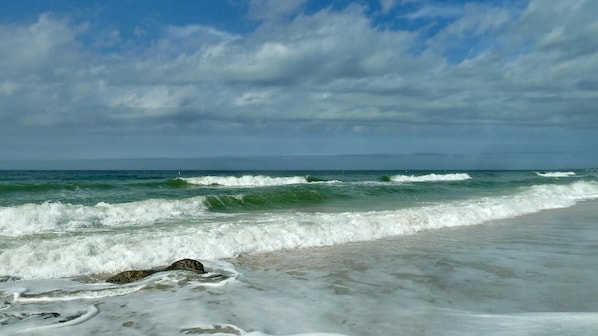 A beach with waves crashing onto the shore and a clear sky above.