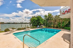 A swimming pool with clear blue water, surrounded by lounge chairs and a view of the water. - Amadeus 7 (Treasure Island)