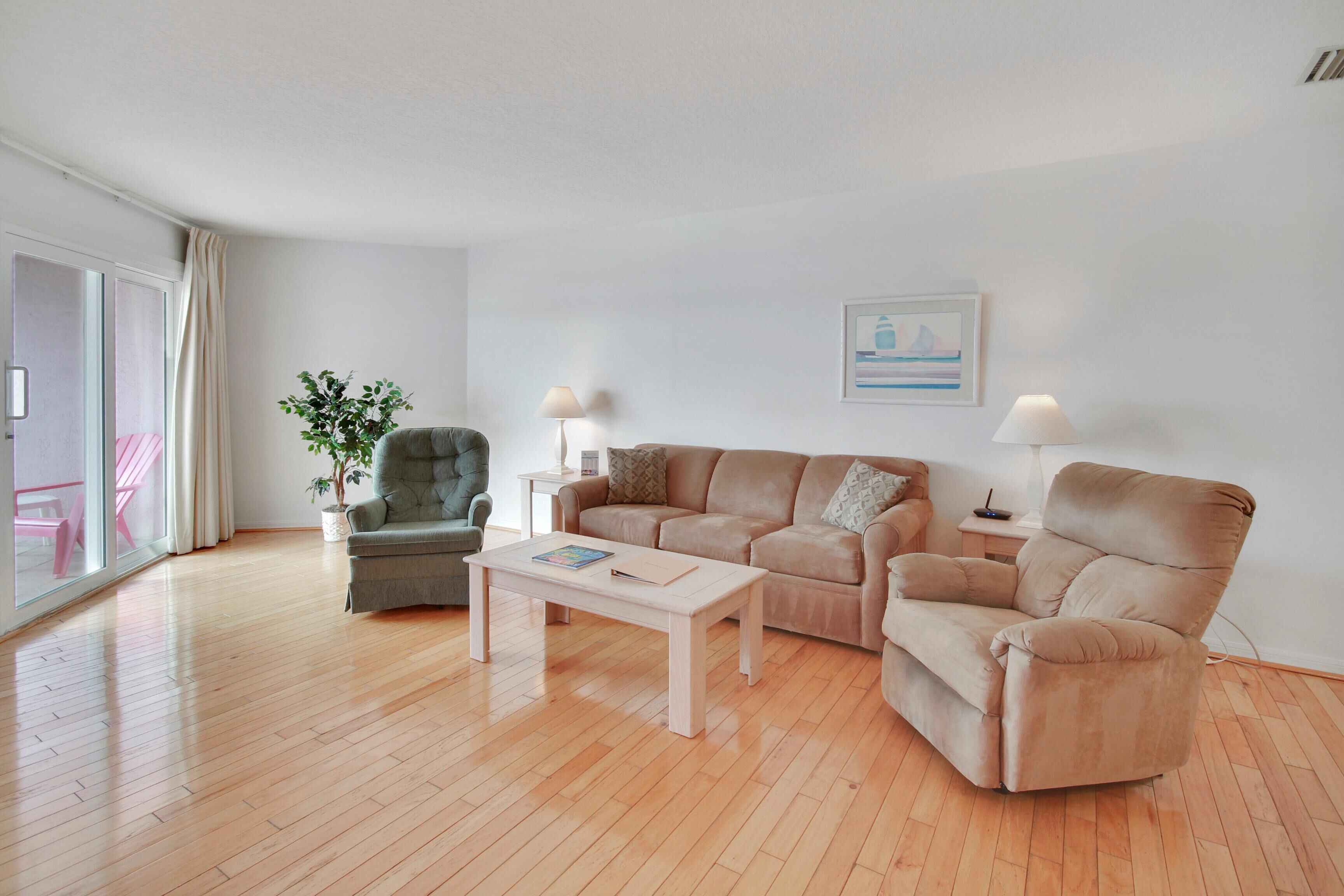 A modern living room with a wooden floor, a beige sofa, a green armchair, a white coffee table, and a potted plant.