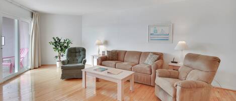 A modern living room with a wooden floor, a beige sofa, a green armchair, a white coffee table, and a potted plant.