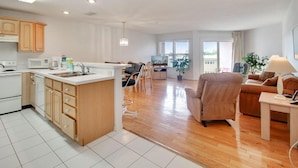 Eine moderne Wohnung mit Küche, Essbereich und Wohnzimmer. Sie verfügt über Holzschränke, eine weiße Arbeitsplatte und ein Sofa.