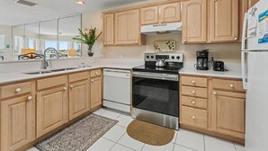 A modern kitchen with wooden cabinets, a stainless steel stove, a dishwasher, and a refrigerator. - Amadeus 9 (Treasure Island)