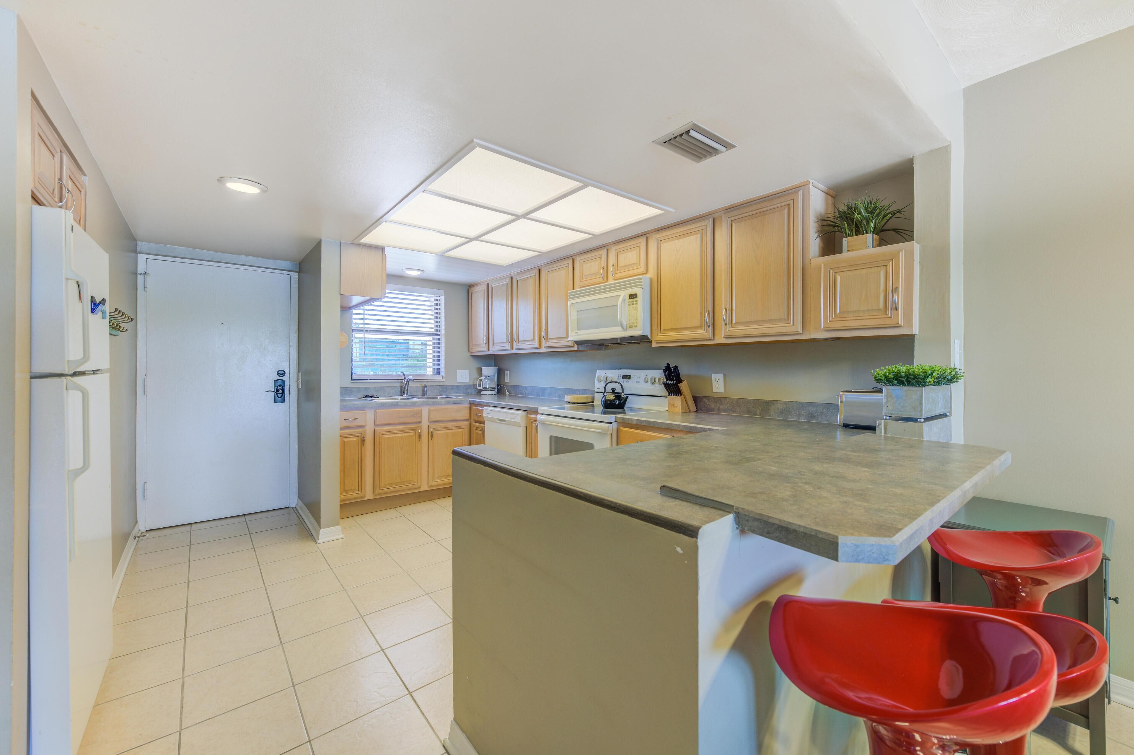 A modern kitchen with wooden cabinets, a built-in microwave, and a large island with red bar stools.