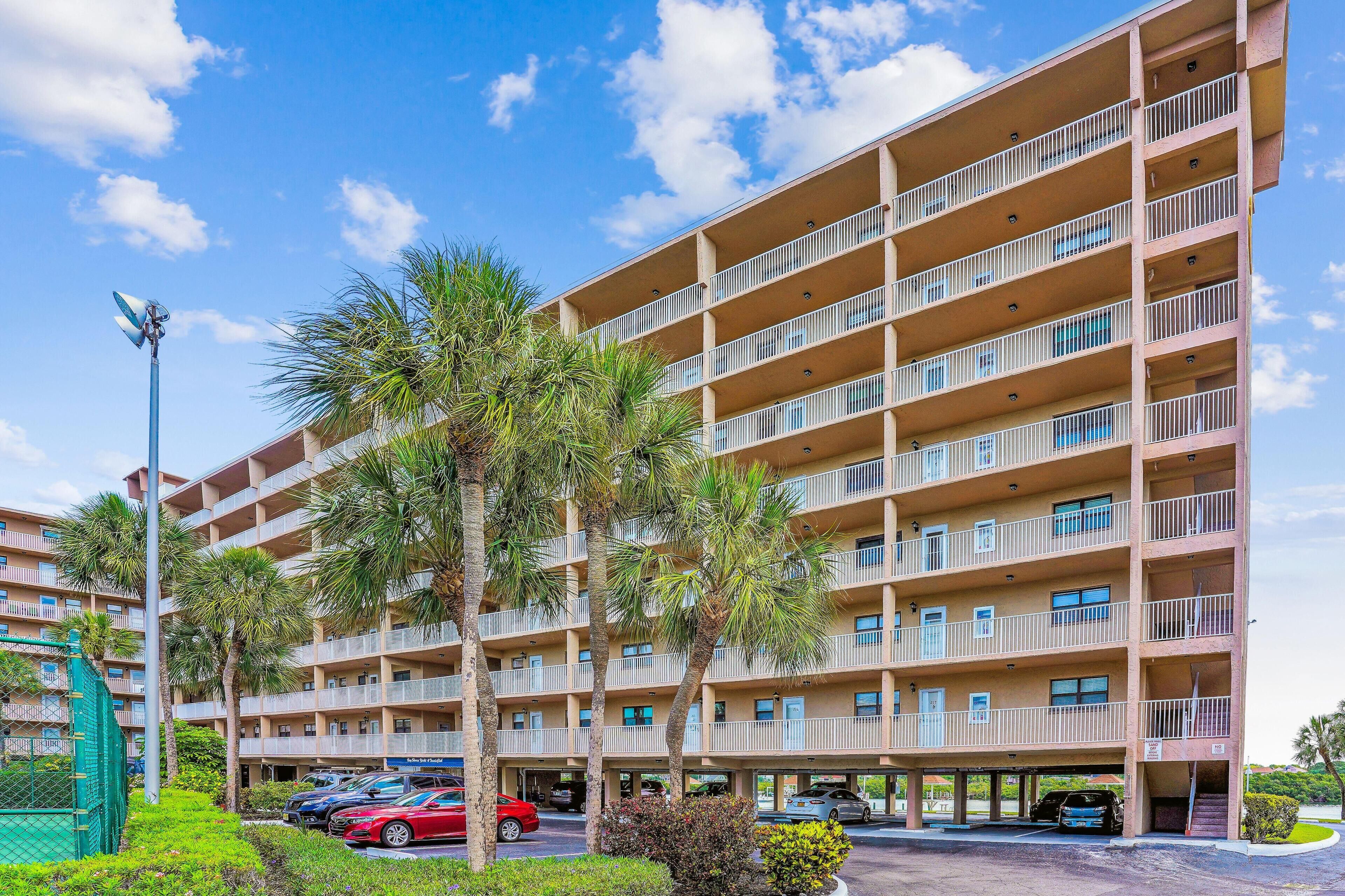 Un hôtel à plusieurs étages doté de balcons, d’un parking et de palmiers.