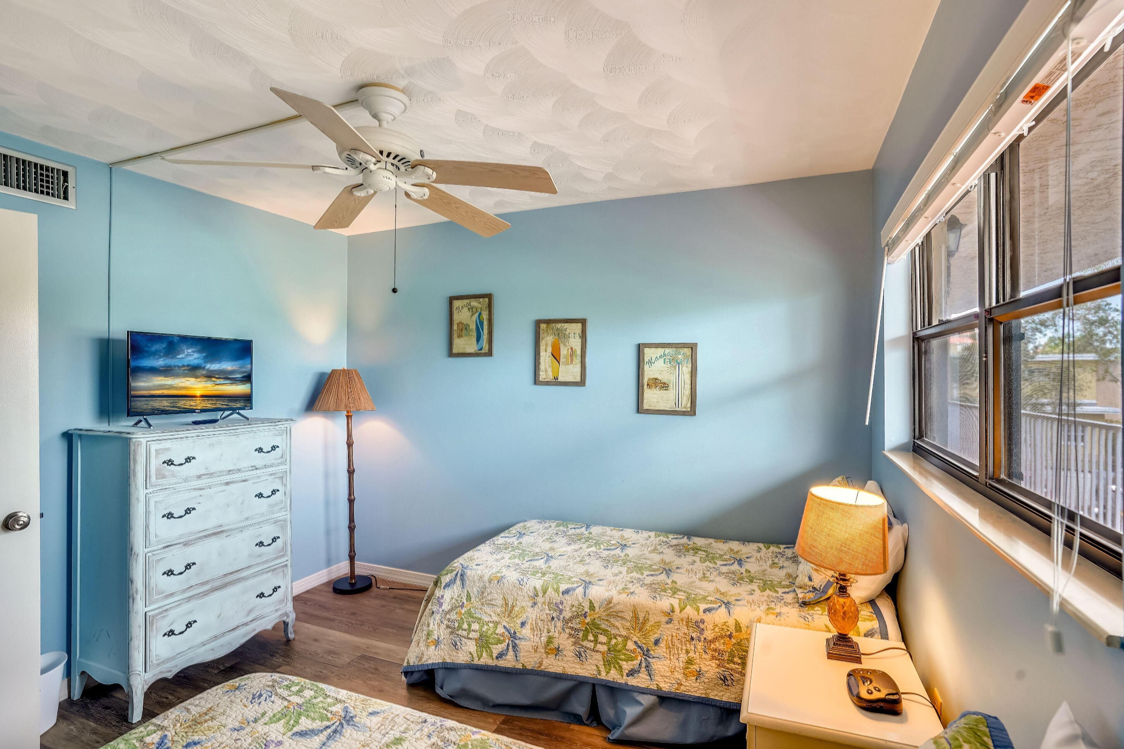 A bedroom with a bed, a dresser, a lamp, and framed pictures on the wall.