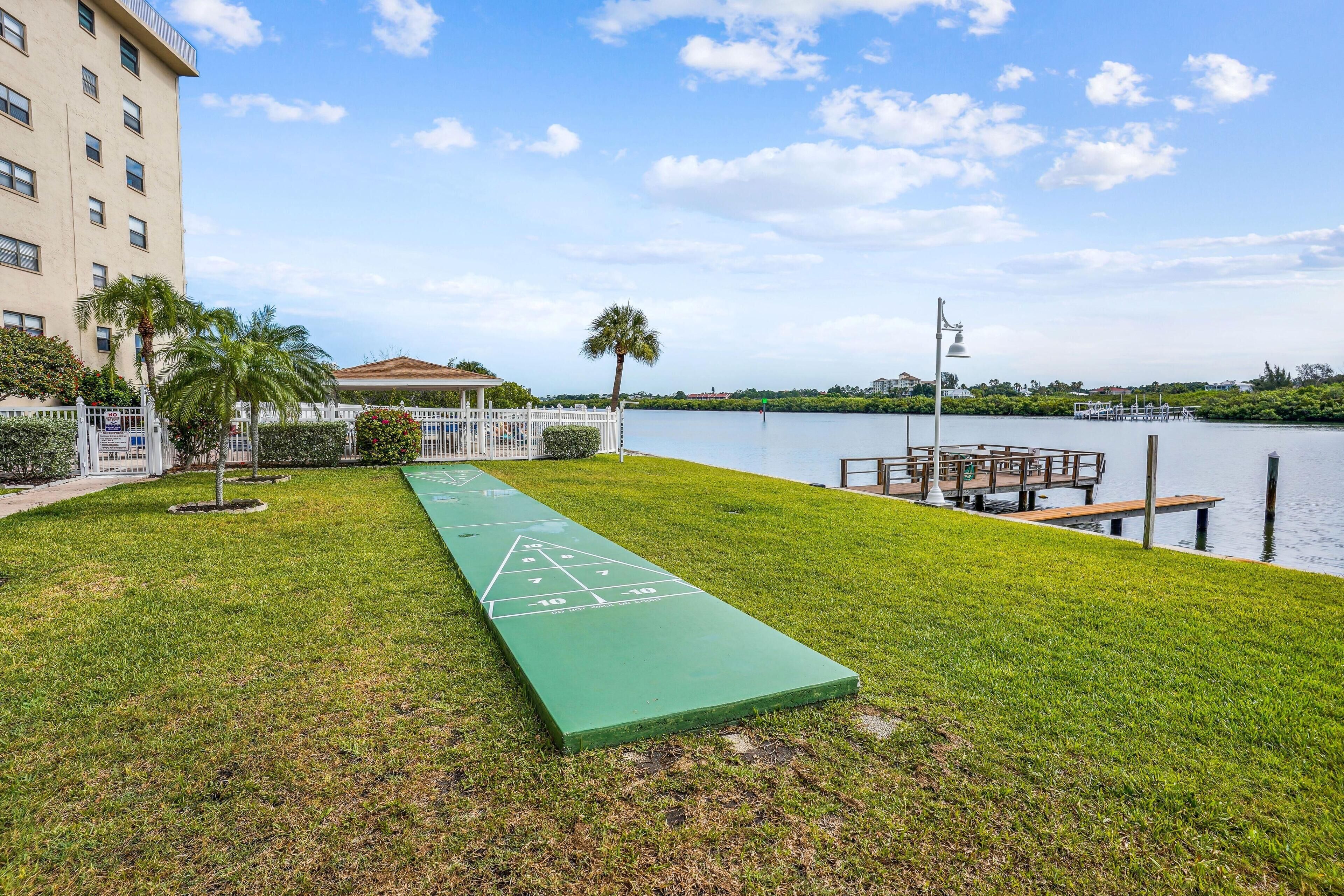 Un campo da shuffleboard verde con una distesa d'acqua e un edificio sullo sfondo.