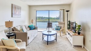 Un salon moderne avec un canapé, des fauteuils, une table basse, un téléviseur et un balcon offrant une vue agréable.