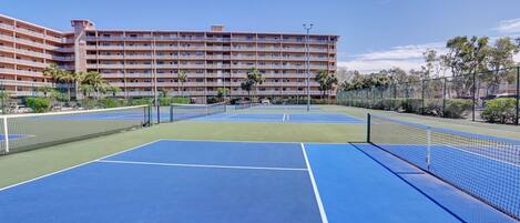 Un terrain de tennis avec un filet, entouré d’une clôture et de palmiers.