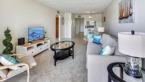 Un salon moderne avec une télévision, une table basse en verre, un canapé et une lampe.