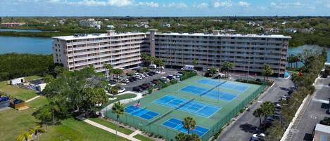 A multi-story hotel with a tennis court and parking area.