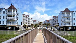 A wooden boardwalk leading to a row of beachfront condominiums with balconies and a clear sky. - Sandy Views - Step Right onto the Sand at Seascape Resort 2/2 condo (Galveston)