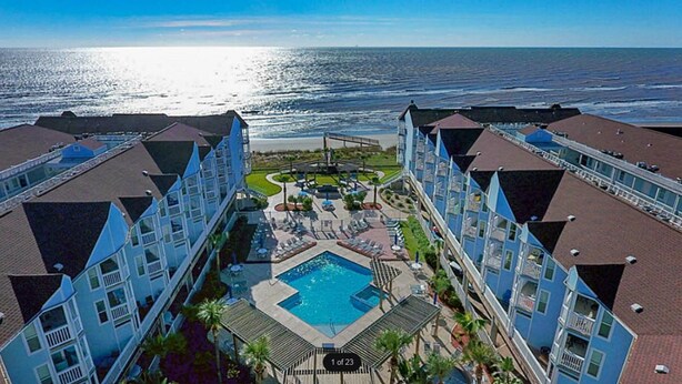 A resort with a central pool, multiple balconies, and a view of the ocean. - Sandy Views - Step Right onto the Sand at Seascape Resort 2/2 condo (Galveston)