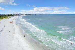A wide beach with clear turquoise waters, a few umbrellas, and a distant city skyline. - Caprice 301 (St. Pete Beach)