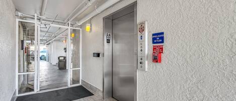 A hallway with an elevator, a fire alarm sign, and a location sign on the wall.