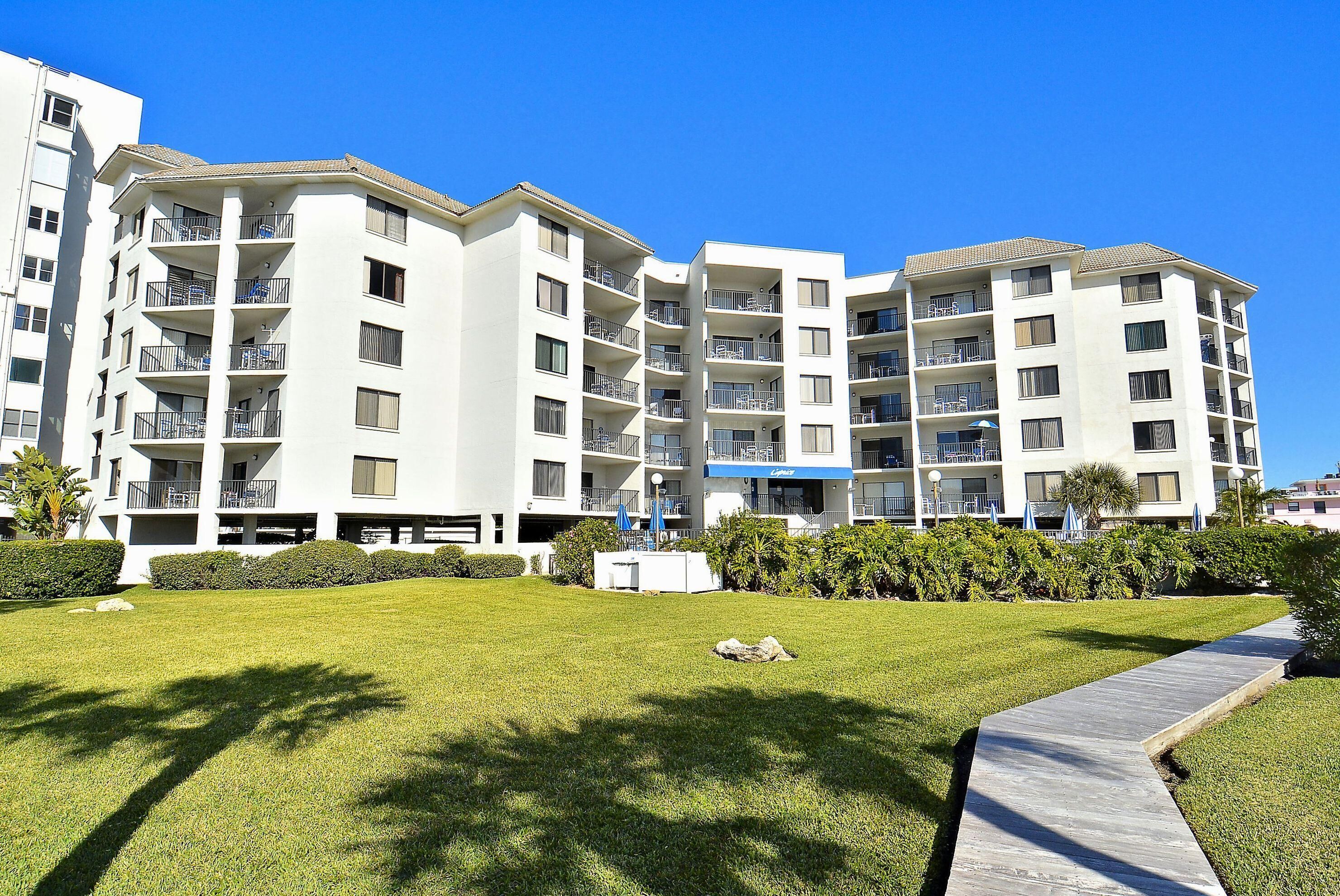 A multi-story residential building with balconies, a well-maintained lawn, and a clear blue sky.