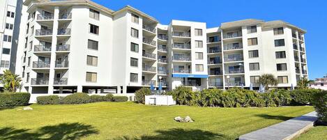 A multi-story residential building with balconies, a well-maintained lawn, and a clear blue sky.