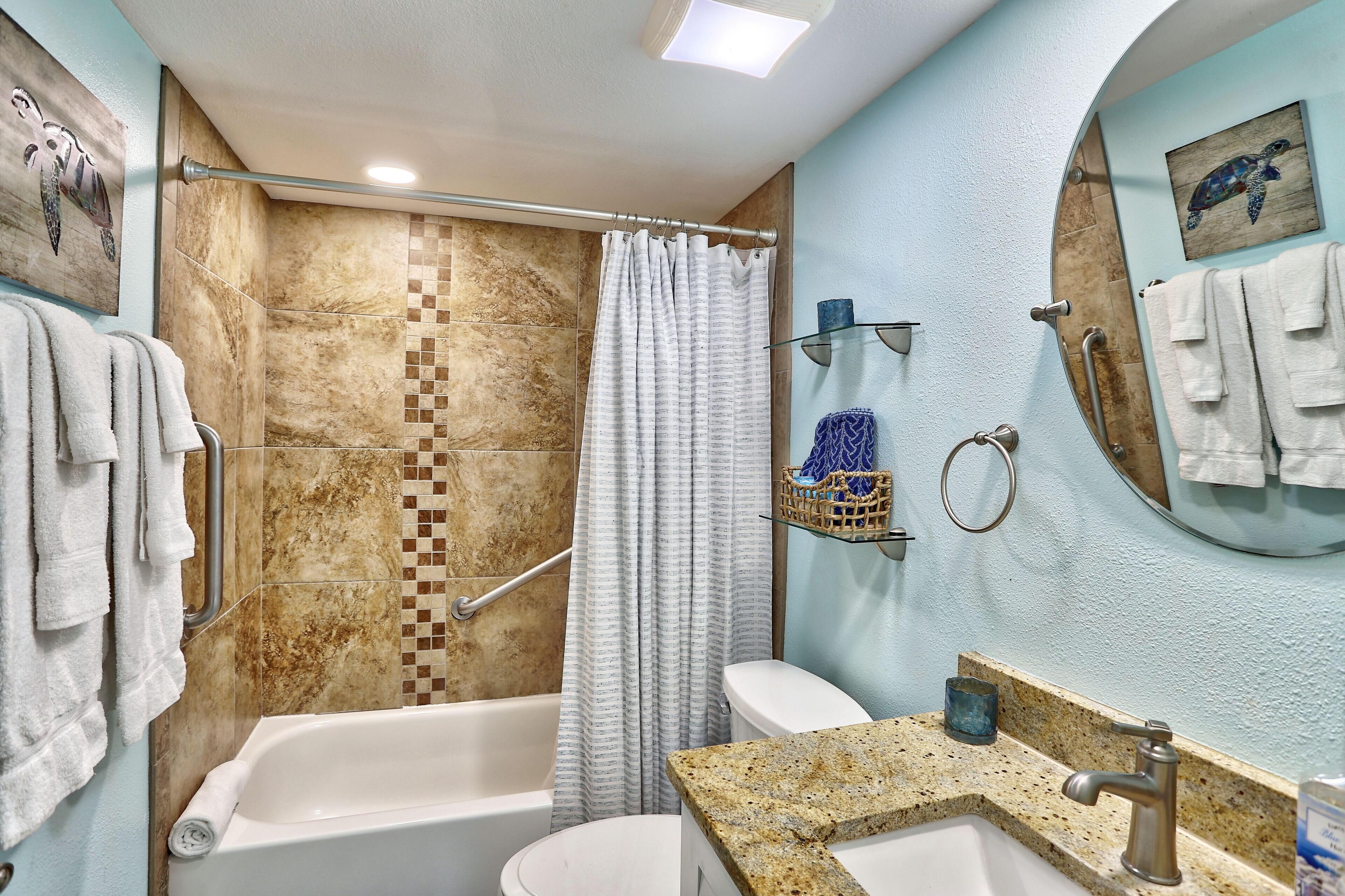 Une salle de bain équipée d’une baignoire, de toilettes et d’un lavabo, avec un rideau de douche, un porte-serviettes et un miroir sur lequel est accrochée une serviette.