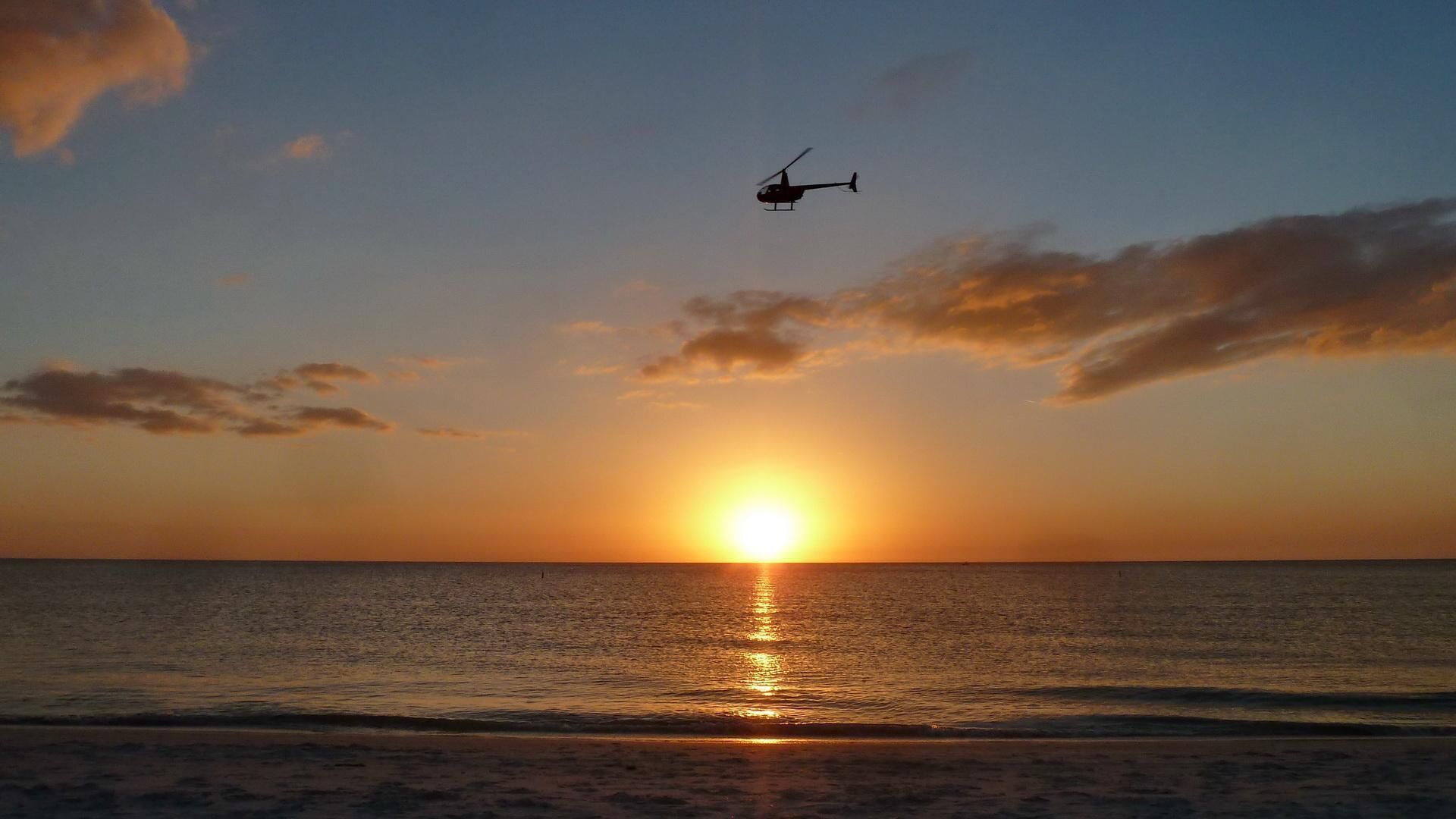 Ein Sonnenuntergang über dem Meer mit einem Hubschrauber am Himmel.