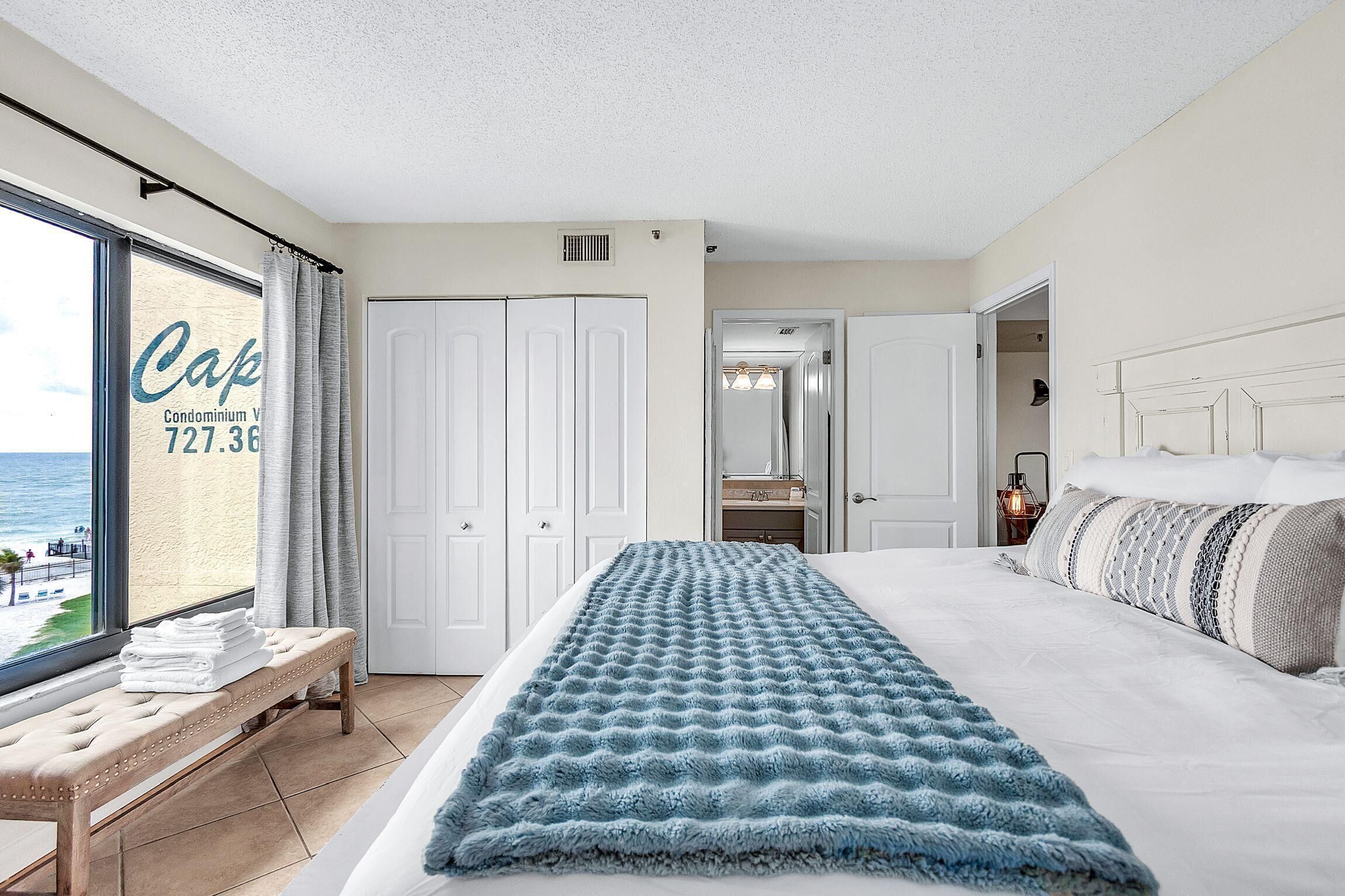 Een slaapkamer met een groot bed, een bankje, uitzicht op het strand en een kledingkast.
