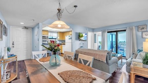 A dining area with a wooden table, chairs, a vase with flowers, and a hanging light fixture. - Caprice 501 (St. Pete Beach)