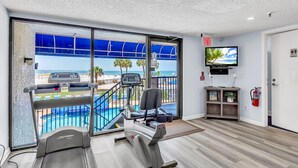 A gym with treadmills and a TV, a fire extinguisher, and a view of a pool and beach. - Caprice 501 (St. Pete Beach)