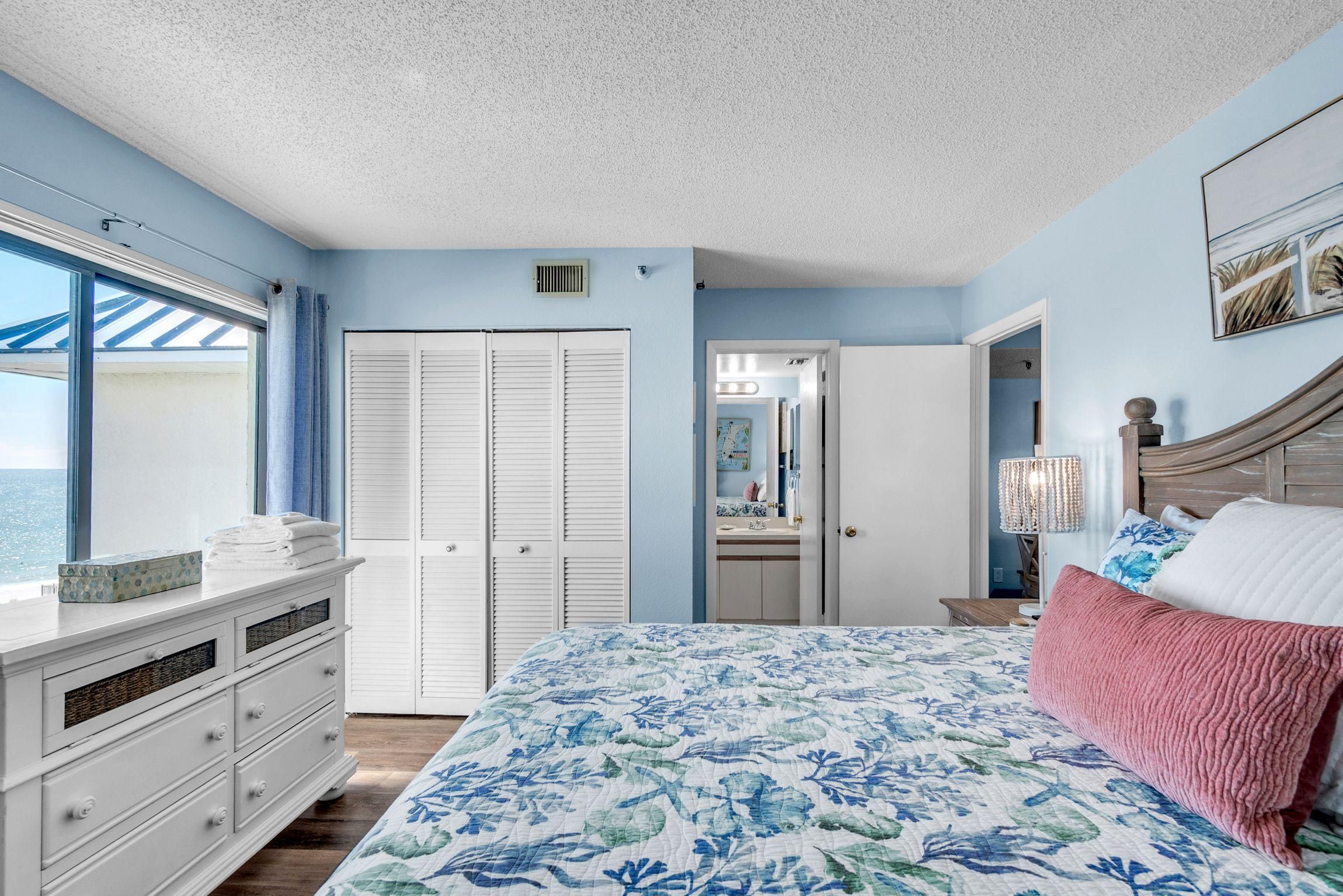 Quarto com cama, cômoda, guarda-roupa e vista para o oceano pela janela.