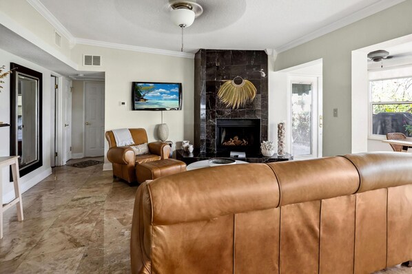 A living room with a fireplace, leather sofas, and a television on the wall.