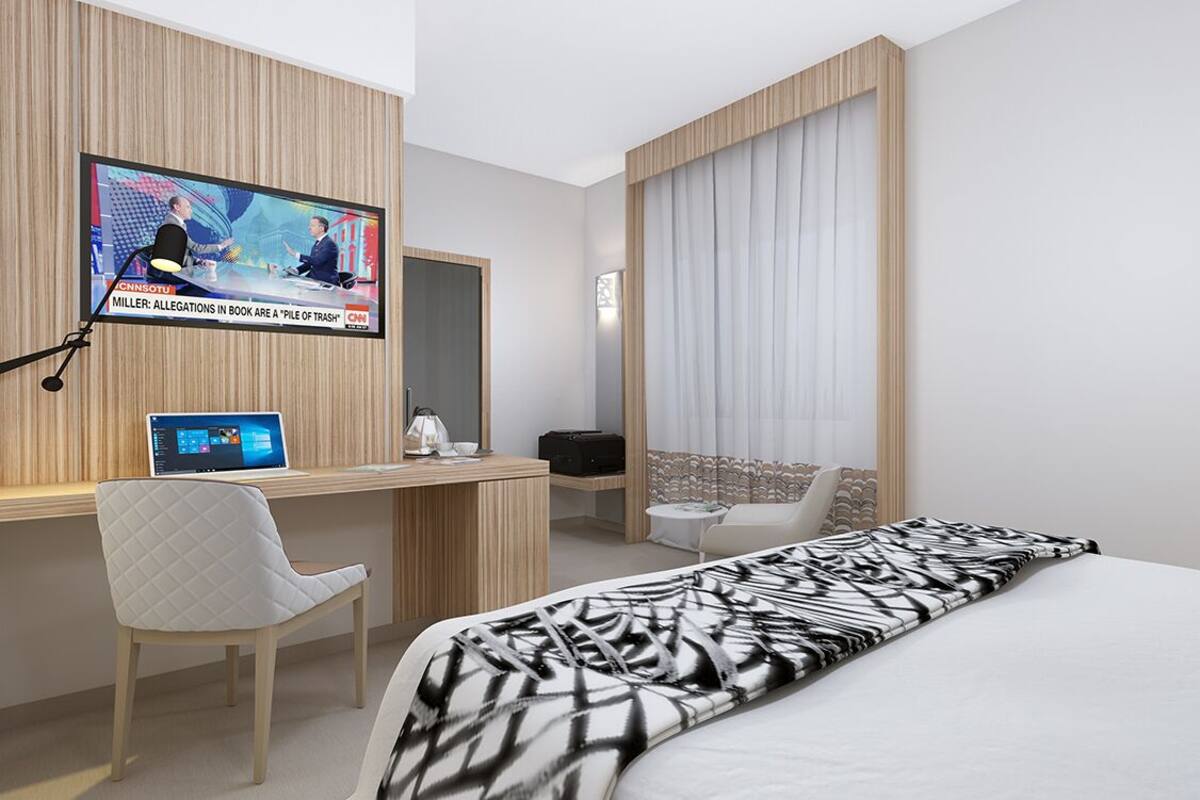 A modern hotel room with a bed, a desk, a chair, a TV, and a window with curtains.