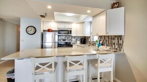 Une cuisine moderne avec des meubles blancs, un îlot central doté de tabourets, un four à micro-ondes, une cuisinière et un réfrigérateur.