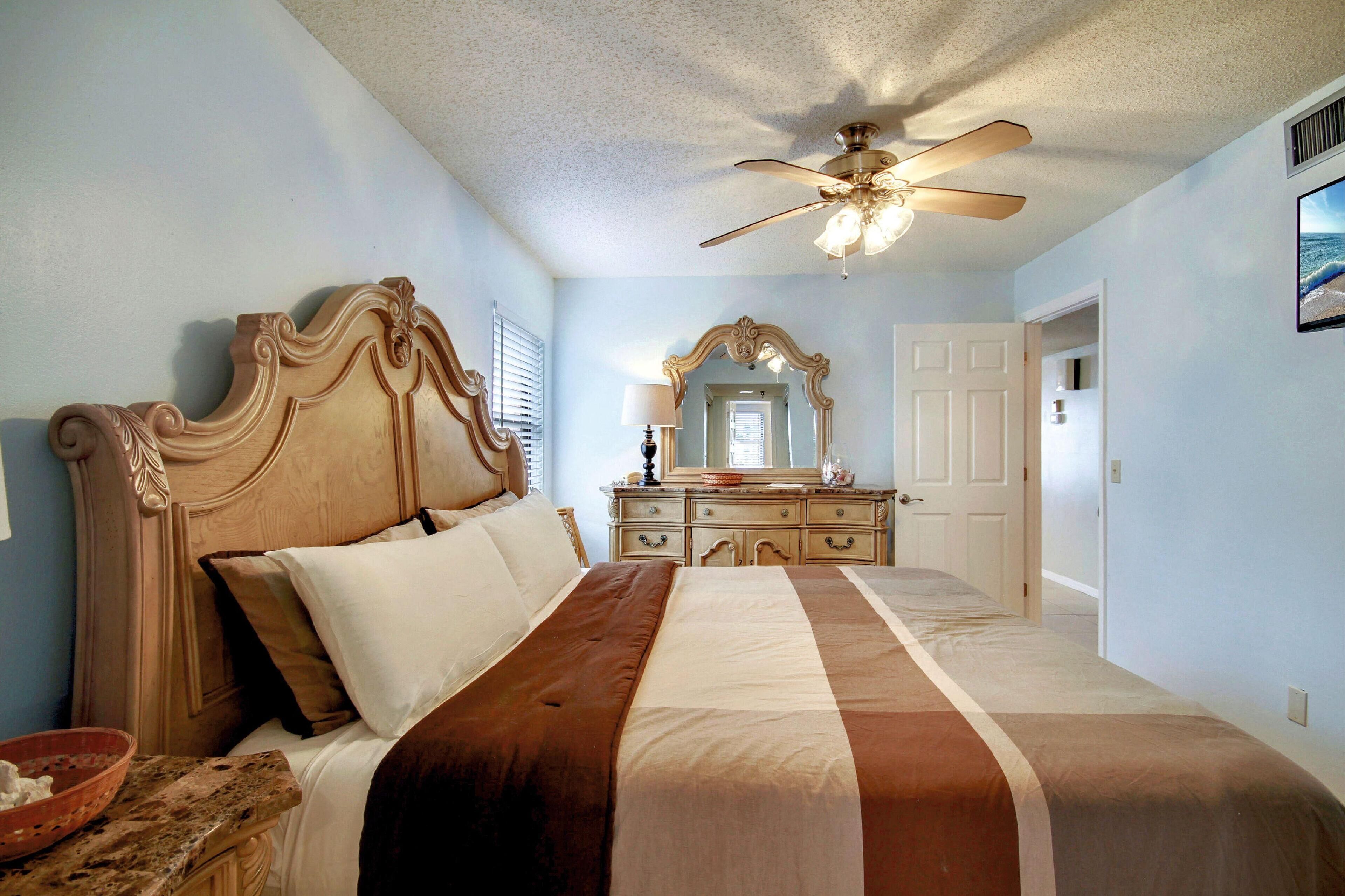 A bedroom with a large bed, a ceiling fan, a dresser, and a mirror.