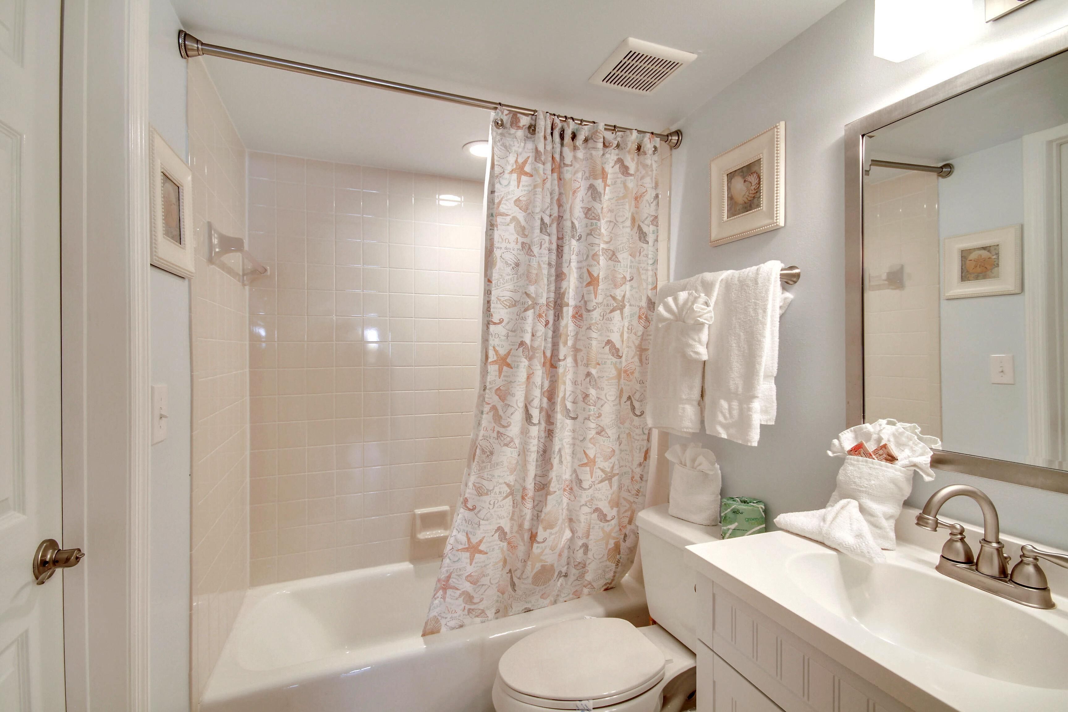 A bathroom with a bathtub, toilet, sink, and a shower curtain with a nautical theme.