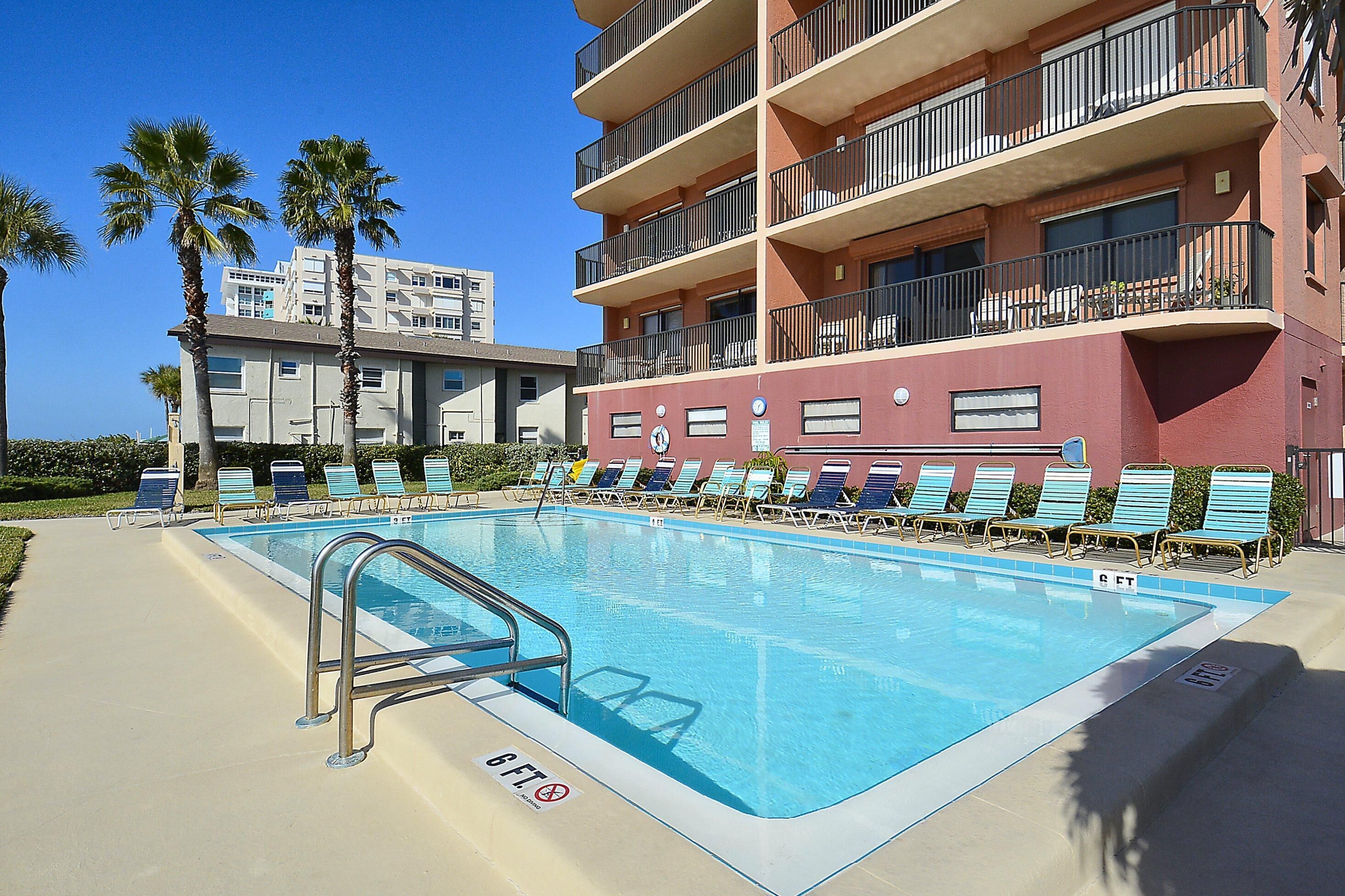 A swimming pool with lounge chairs, a pool ladder, and a building with balconies.