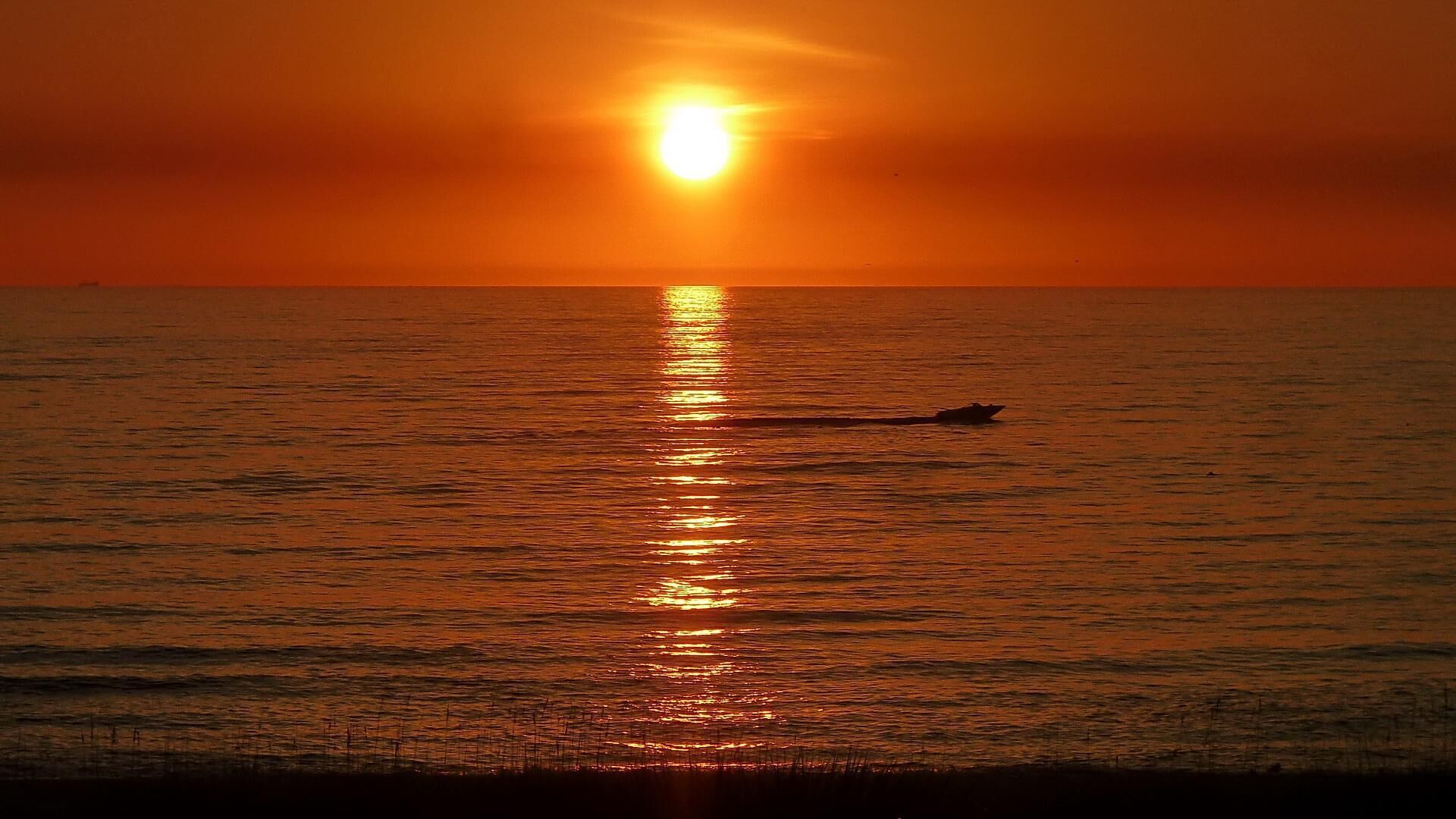 Een zonsondergang boven een kalme zee, met een boot in de verte.