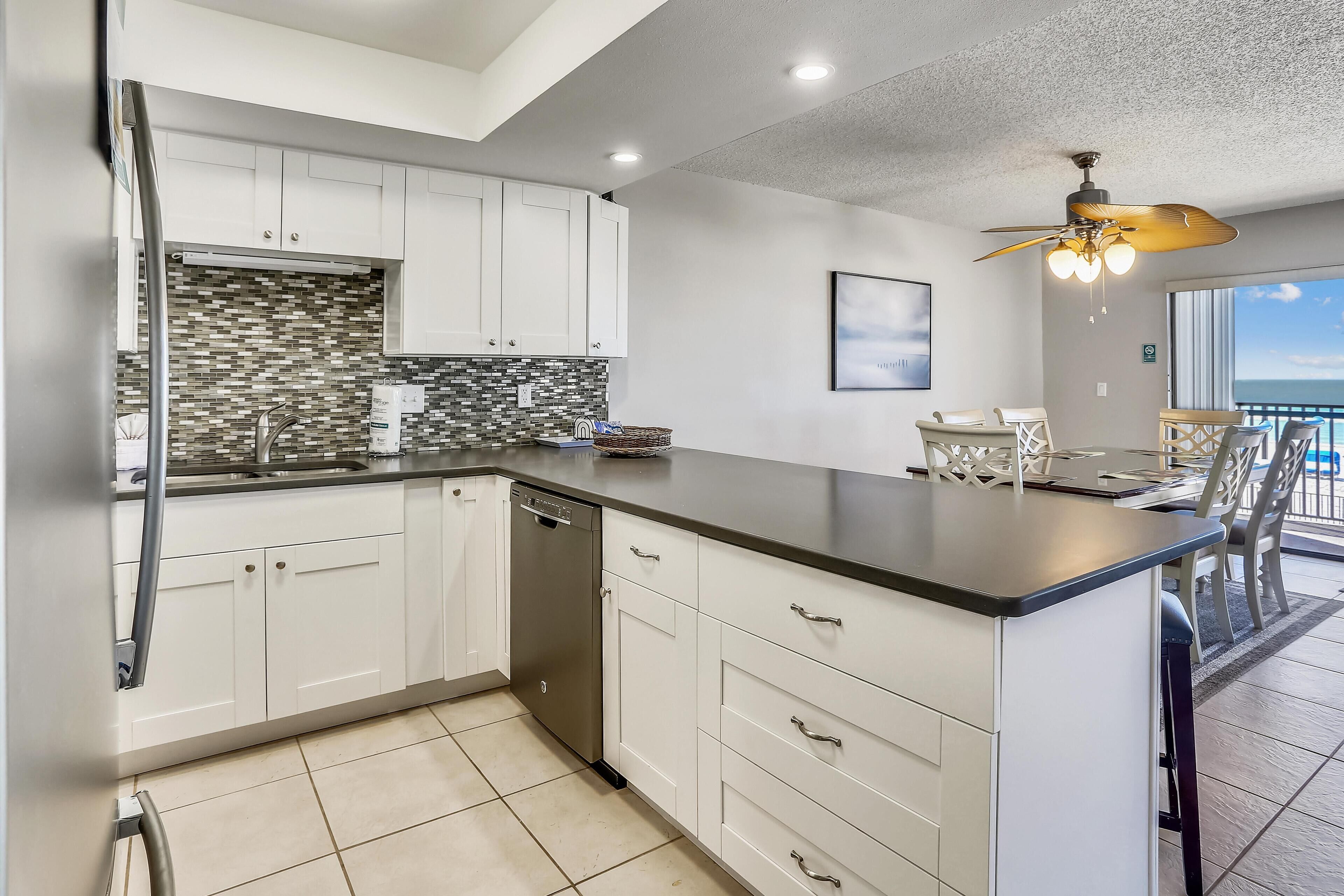A modern kitchen with white cabinets, a black countertop, and a tiled backsplash.