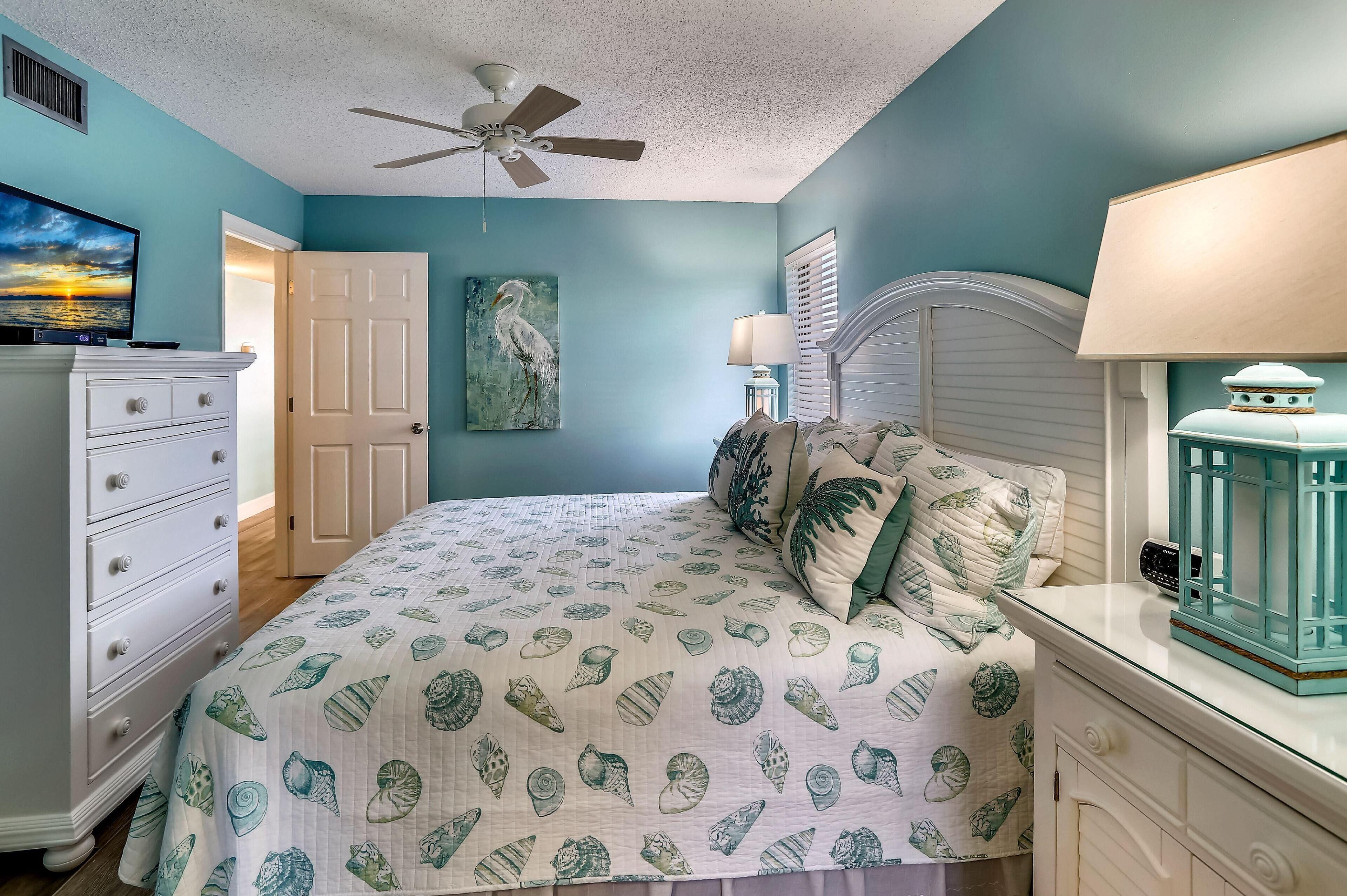 A bedroom with a bed, dresser, nightstand, lamp, and ceiling fan.