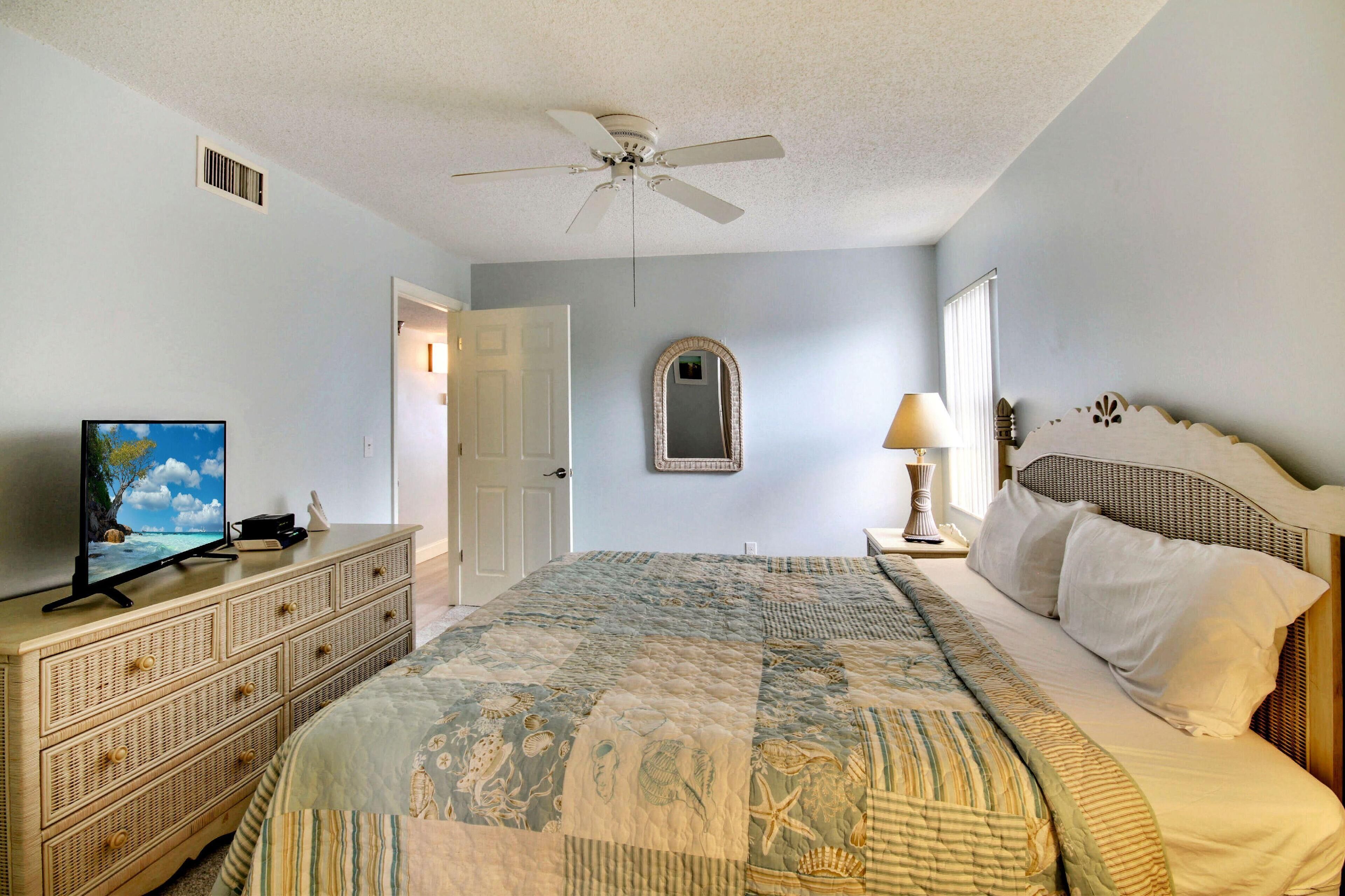 A bedroom with a large bed, a ceiling fan, a dresser, a television, and a mirror.