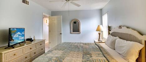 A bedroom with a large bed, a ceiling fan, a dresser, a television, and a mirror.