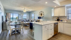 A spacious living area with a dining table, a sofa, and a kitchen with white cabinets and a dishwasher. - Emerald Isle 204 (North Redington Beach)