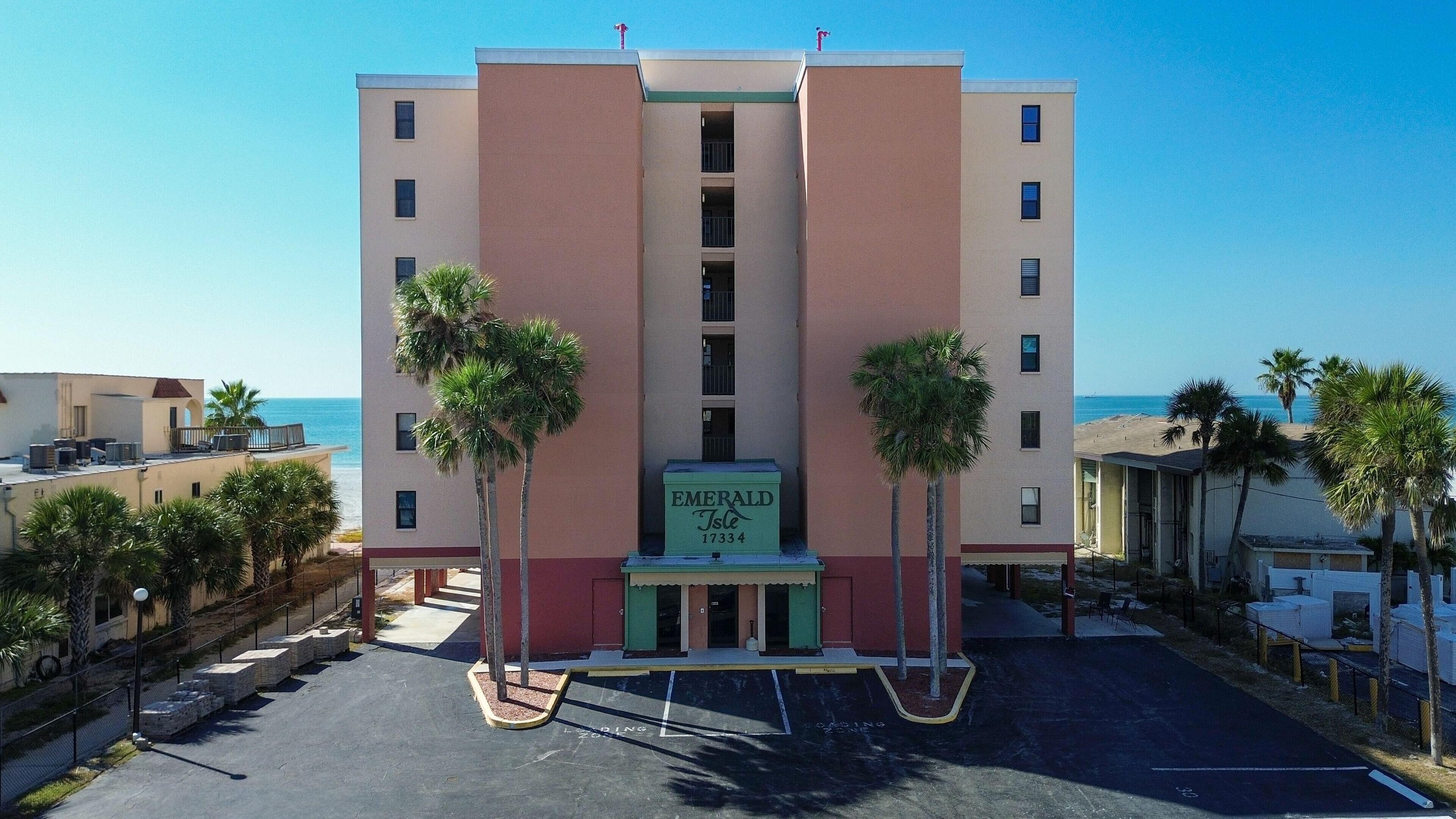 A multi-story hotel with a central entrance, palm trees in front, and a view of the beach.
