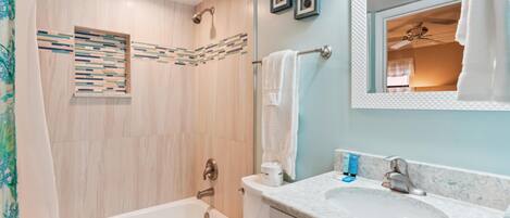 A bathroom with a bathtub, a sink, and a shower. There are towels and toiletries on the counter.
