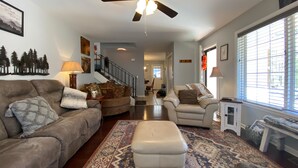 A spacious living room with a ceiling fan, a patterned rug, and a staircase leading to another level.