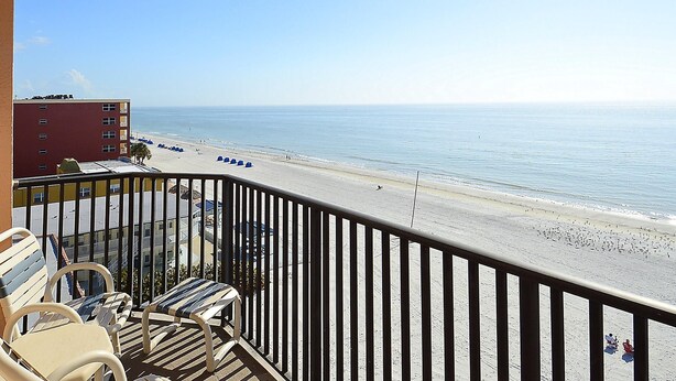 A balcony with a view of a beach, chairs, and a building in the background. - Emerald Isle 601 (North Redington Beach)
