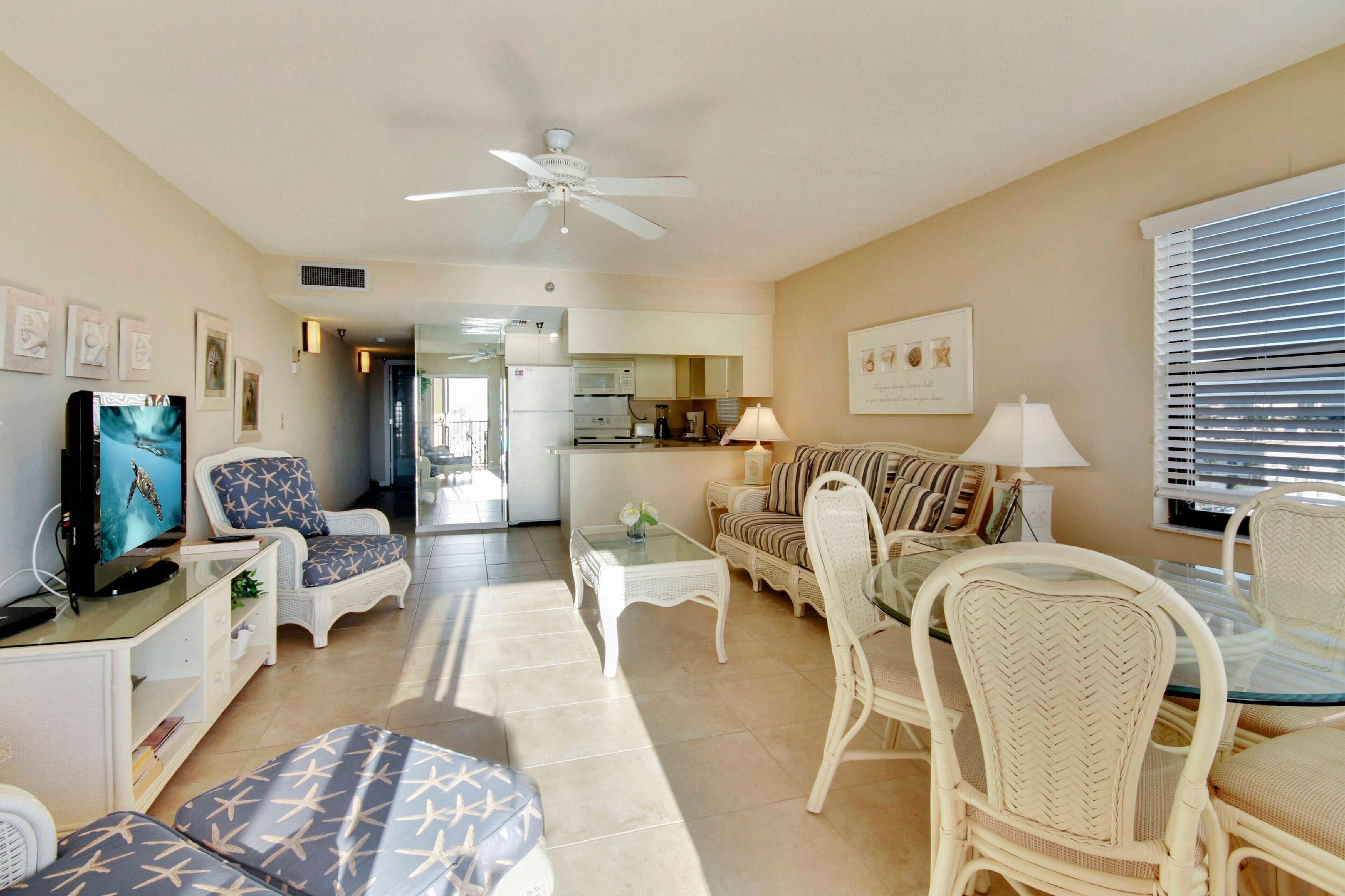 A spacious living room with a television, seating area, and a kitchen in the background.