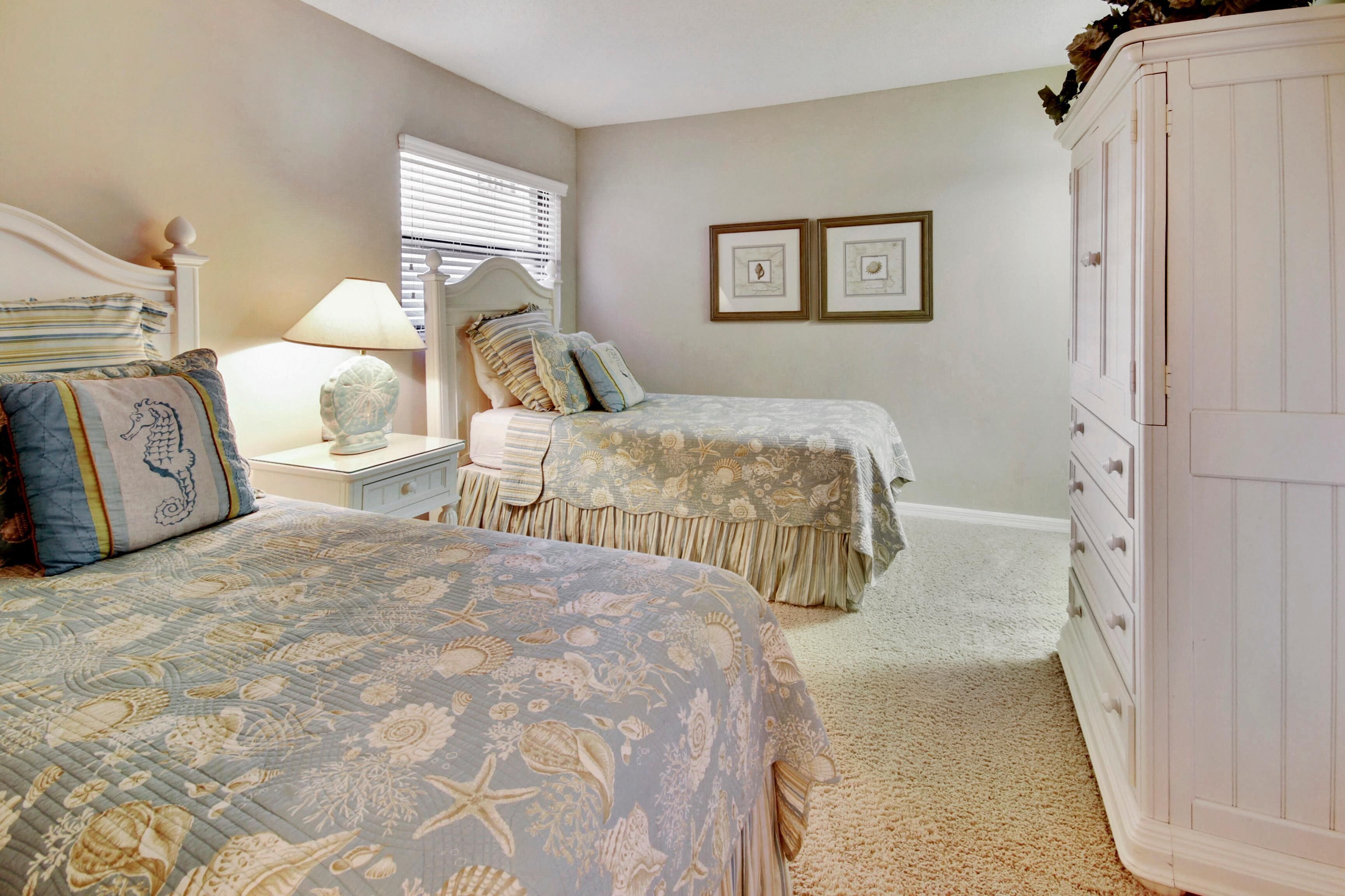A bedroom with two beds, a nightstand, a lamp, and a wardrobe.